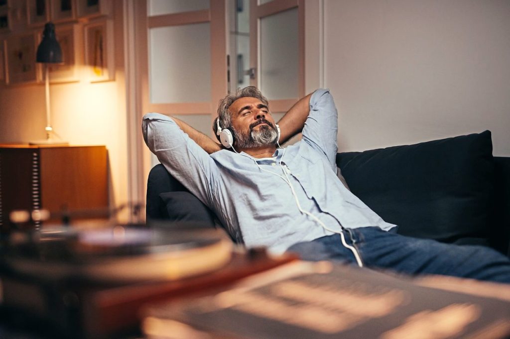 mid aged man listening music with headphones on phonograph, relaxed in sofa at his home